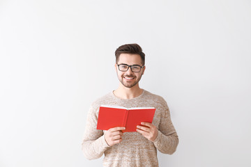 Handsome young man with book on light background