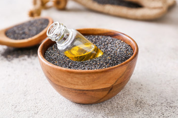 Bowl with poppy seeds and bottle of oil on table