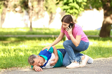 Female passer-by calling an ambulance for mature man who is having heart attack outdoors