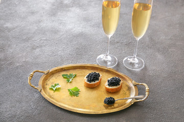 Tray with delicious caviar and glasses of champagne on grunge background