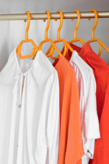 Coral and White colour clothes on hangers. Several blouses, shirts for casual outfit. Fashion store background.