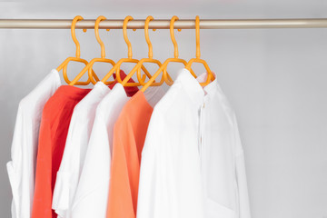 Coral and White colour clothes on hangers. Several blouses, shirts for casual outfit. Fashion store background.