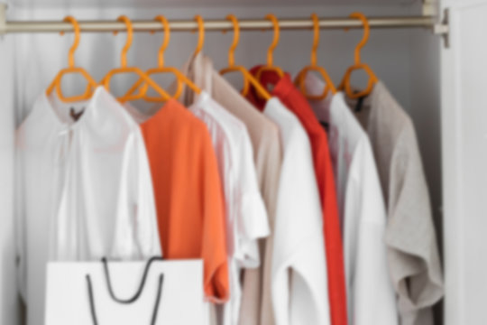 Collection of clothes hanging on rack in wardrobe in dressing room and white paper shopping bag. Fashion shopping concept background.