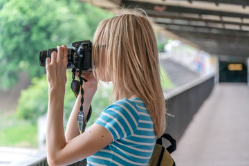 Blonde girl takes pictures on the camera on the bridge in sunny weather