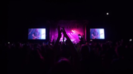 concert party, crowd of fans jumping and clap into rhythm at rock festival with phones into hands in spotlight lighting