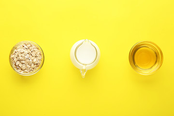Bowls with oat flakes, honey and milk in jug on color background