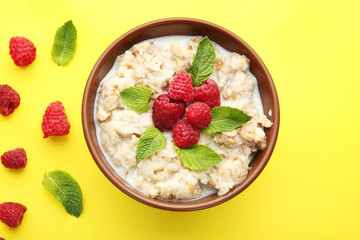 Bowl with tasty sweet oatmeal and raspberry on color background