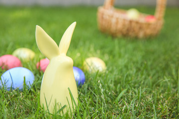 Ceramic bunny with colorful Easter eggs on grass outdoors