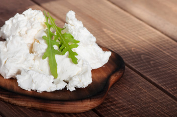 Cottage cheese on the old wooden background, decorated with arugula.