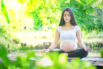 Pregnant woman doing yoga exercise in nature on a summer