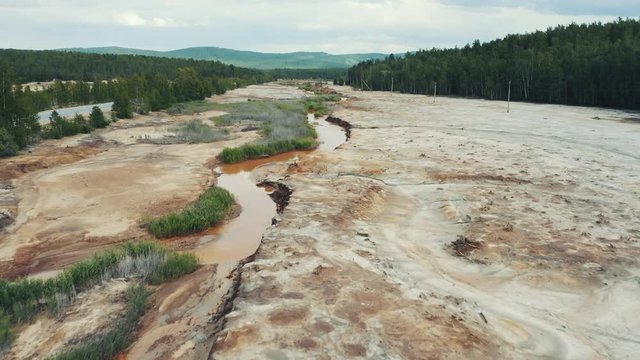 Aerial view; drone flying forward over a polluted river with destroyed ecosystem and copper tailing dump poisoning ground and water; air emissions from industry; environmental disaster in South Ural