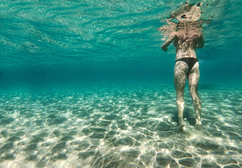 A woman swimming and walking on the sandy bottom of the sea. A girl underwater and turquoise ocean...