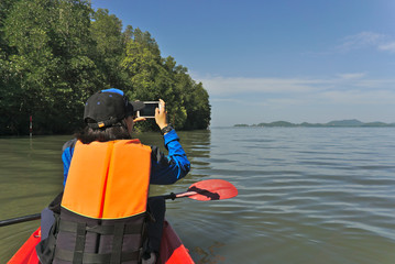 Female asian traveller wearing orange vest life jacket is using smart phone taking photo of the...