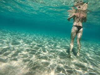 A woman swimming and walking on the sandy bottom of the sea. A girl underwater and turquoise ocean around.