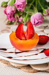 Ripe apricot and sweet strawberries with chocolate sauce on a white plate.