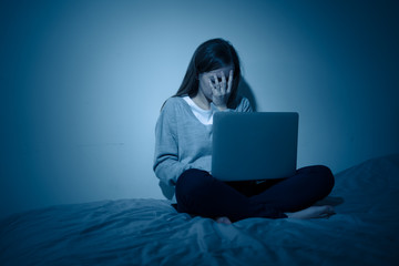 Sad teenager girl with laptop suffering bullying and harassment online. Cyberbullying concept.