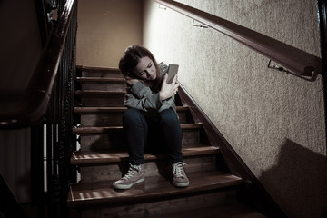 Sad depressed unhappy teenager girl suffering from cyberbullying by mobile smart phone sitting alone.