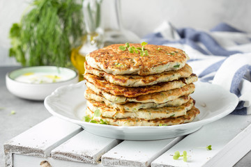 Chicken pancakes with zucchini and herbs, stack of cutlets on plate. Delicious summer food, healthy lunch with meat, vegetables, yogurt sauce