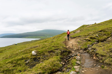 Hiking path above Leitisvatn lake with tourist silhouette. Vagar, Faroe Islands.