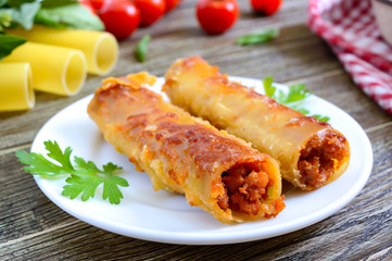 Stuffed cannelloni with bechamel sauce. Cannelloni pasta baked with meat, cream sauce, cheese on a wooden background.