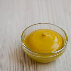 Homemade organic mustard in a glass bowl on a white wooden surface, low angle view. Close-up.