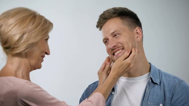 Mother pinching cheeks to infantile adult son under mom overprotection, care