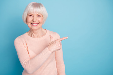 Portrait of pretty lady pointing at copy space smiling wearing pastel jumper isolated over blue...