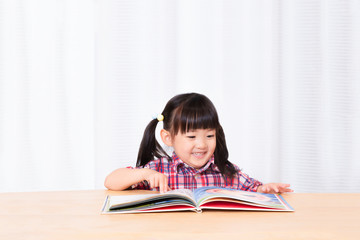 白背景の前で笑顔で絵本を読む幼い女の子。幼児、教育、読書、学習、成長、育児イメージ