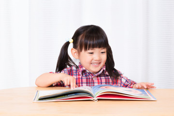 白背景の前で笑顔で絵本を読む幼い女の子。幼児、教育、読書、学習、成長、育児イメージ