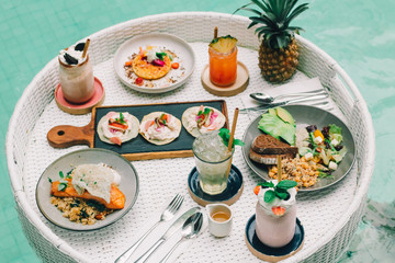 Breakfast on floating table in the pool. Healthy food with smoothie and Pineapple.
