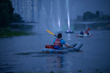 Man rowing canoe in the evening, illuminated fountains on a background