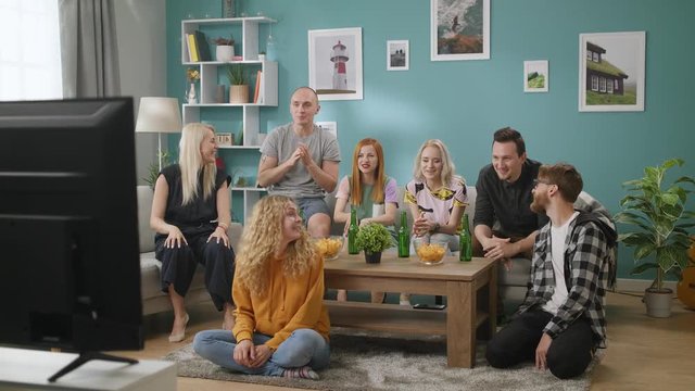 In the Living Room Group of Friends on Watching TV, And Drinks Beer With Snacks