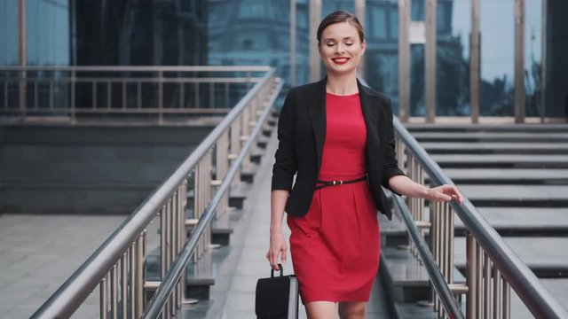 portrait of a young woman in a jacket and carrying a briefcase in her hands. self-confident business woman in a red dress walks against the backdrop of modern buildings