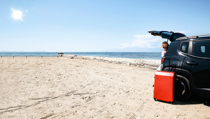 A woman in a black car on a sandy beach and blue ocean view.