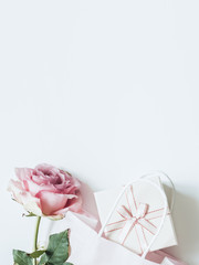 Pink pstel rose, light paper bag and light gift box with a bow on a white background. Gentle romantic wedding or womens day headline. Wide banner spring sale, desaturated colors top view.