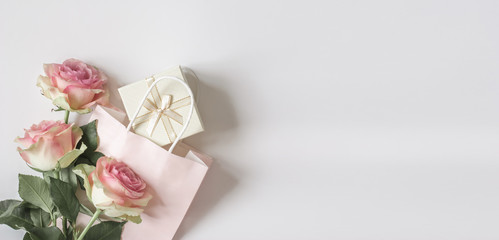 Top view composition with pastel pink three roses, paper bag and light gift box with a bow on a...