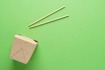 Kraft paper container and chopsticks on green background.