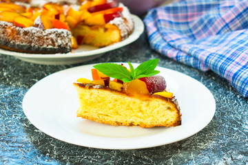  A piece of cake with peaches and plums decorated with a leaf of mint on a plate. Preparing a dissert.