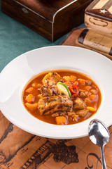 Beef stew with potatoes on white plate on old map background