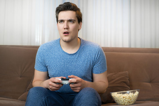 young handsome man playing video game sitting on comfy sofa looking fascinated