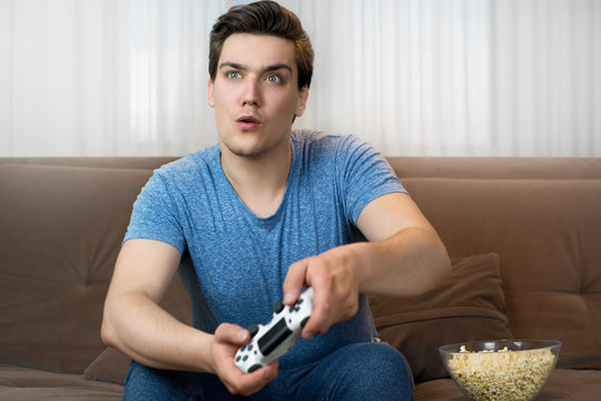 young handsome man playing video game sitting on comfy sofa looking involved in mission