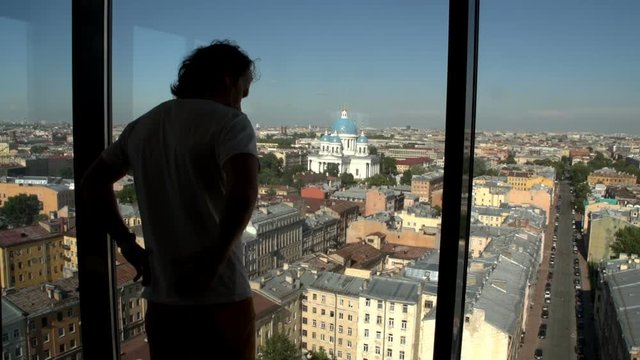 Silhouette of man watching across the window. Young man watching cityscape across panoramic window in skyscraper