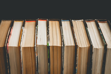Stack of old books, textbooks on a black background, classic literature. Books in a row on a dark background