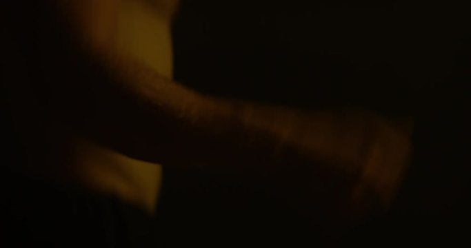 Male Body Builder Skipping In A Dark Room, Training For Fitness Competition.Warming Up Before Work Out, Cardio Session. Dim Lit Room, Yellow Light On Him. Close- Up Of Hand.