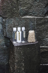 Different bottles with shampoo, gel and conditioner with natural organic washcloth on stone shelf in outdoor shower. Close up.