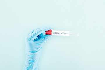 Obraz premium cropped view of doctor in latex glove holding empty test tube with allergy test lettering isolated on blue