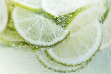 Close-up fresh lemon slices in cold lemonade with bubbles. Summer tropical beverage - obrazy, fototapety, plakaty