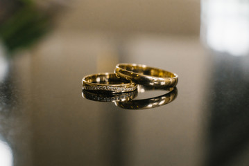 gold wedding rings for the bride and groom with diamonds pebbles, close-up on the mirror surface of brown and gray