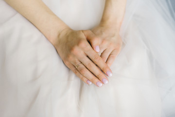 Fototapeta na wymiar the bride's hands are folded and lie on the wedding dress, wedding manicure and wedding ring on the finger