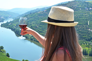 Girl with a glass of wine looking to the vineyards in Douro Valley, Portugal